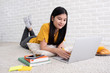 © weedezign - Asian female freelancer working on laptop computer at home.woman lying down on carpet at brick wall.working online lifestyle.