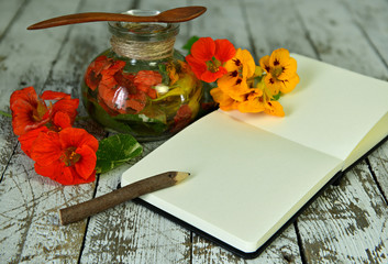 Nasturtium flowers in glass bottle and open diary with pencil on wooden table.