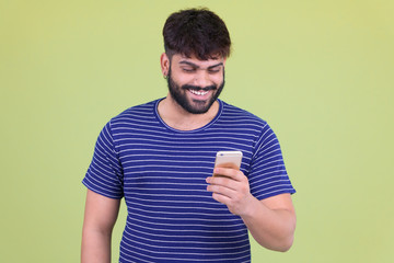 Happy young overweight bearded Indian man using phone