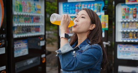 Wall Mural - Woman drink a bottle of juice at vending machine