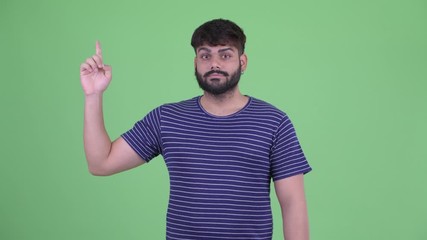 Wall Mural - Happy young overweight bearded Indian man pointing up