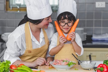 Wall Mural - Asian woman young mother with son boy cooking salad food  with vegetable holding two carrots and tomatoes, bell peppers for happy family cook food enjoyment lifestyle kitchen