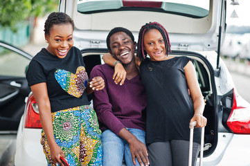 Three african american friends sit in the trunk of the car.