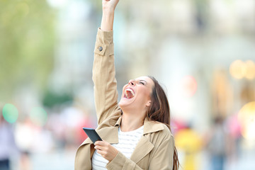 Poster - Excited woman holding phone celebrating good news outdoors