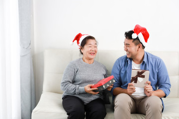 Wall Mural - Asian senior woman mother and young man son in blue shirt give gift box for Christmas gift in living room