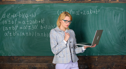 Wall Mural - Lady teacher wear eyeglasses holds laptop surfing internet. Teacher blonde woman with modern laptop surfing internet chalkboard background. School innovation. Distance education concept