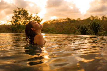 Wall Mural - tropical holidays lifestyle portrait of young beautiful and happy Asian Korean woman in bikini enjoying sunset at amazing jungle resort infinity pool swimming relaxed