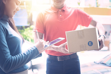 Wall Mural - Beautiful girl receiving parcel from postman and signing on tablet that delivery goods to home's customer