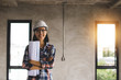 © khwanchai - portrait of engineering women at construction site with worker working behind background