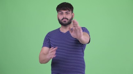 Wall Mural - Stressed young overweight bearded Indian man with stop gesture