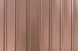 Metal wall siding texture. Ribbed, striped surface. Shiny metallic cladding on wall. Brown background. Reflected light cover.