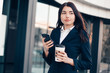© zadorozhna - Successful smiling businesswoman or entrepreneur using phone and drink coffee standing in front of his office.
