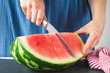 Female hands cutting big ripe watermelon with red flesh into even slices with knife