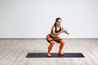 © khosrork - Portrait of young sporty healthy beautiful woman in black top and orange leggings doing squatting with elastic resistance band. Isolated, white wall, indoor, workout concept, looking away