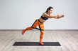 © khosrork - Side portrait view of beautiful young woman wearing black tank top and orange leggings, workout alone against white wall, doing yoga or pilates exercise with latex resistance band. Full length, indoor