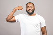 © denis_vermenko - Close up portrait of a happy young african american man flexing bicep muscle isolated against grey background.