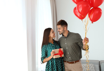 Wall Mural - Young couple with air balloons and gift box at home. Celebration of Saint Valentine's Day