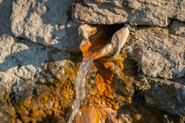 Wall Mural - Close up view of a water fountain. Water coming from a hole on the wall covered with algae.