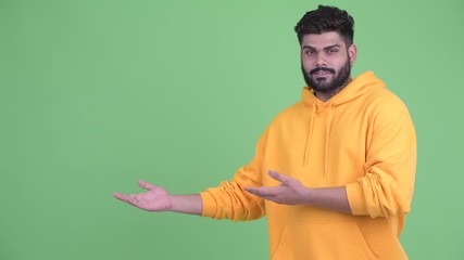 Wall Mural - Happy young overweight bearded Indian man showing something