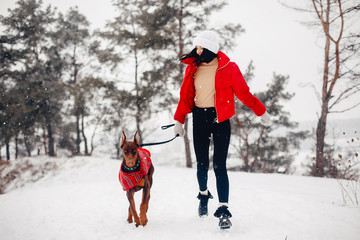 Wall Mural - Cute girl walking in a winter park. Woman in a red jacket. Lady with a dog