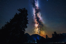 Milky Way Galaxy In Universe Astrophotography. Silhouettes Of Mountains And Trees. Stars And Nebula At Night Sky Landscape