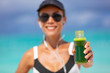 © Maridav - Healthy fit woman showing sports green juice smoothie drink for weight loss detox cleanse. Happy smiling athlete girl holding glass bottle drinking breafkast outside in summer outdoors.