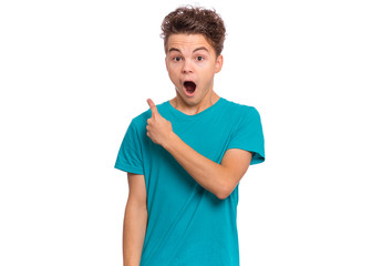 Wall Mural - Portrait of teen boy pointing to back behind with hand and finger, isolated on white background. Cute young surprised teenager attracted by attention pointing finger at something. Shocked child.