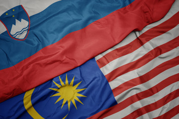 waving colorful flag of malaysia and national flag of slovenia.