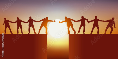 Fotomural Concept du travail d’équipe avec deux groupes d’hommes, séparés par un gouffre qui tente de se rejoindre en se tenant mutuellement pour réussir à surmonter l’obstacle