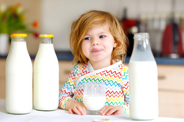 Wall Mural - Adorable toddler girl drinking cow milk for breakfast. Cute baby daughter with lots of bottles. Healthy child having milk as health calcium source. Kid at home or nursery in the morning.