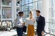 © Wavebreak Media - Young business people stand using laptop in modern office lobby
