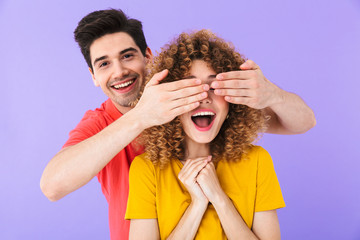 Wall Mural - Photo of cheerful couple, man smiling and covering woman's eyes standing behind her