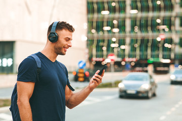 Young sport man walking around in the city and listens to music via smartphone through wireless headphones