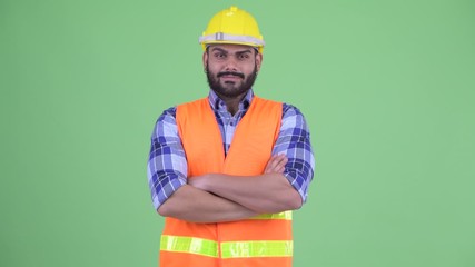 Wall Mural - Happy young overweight bearded Indian man construction worker smiling with arms crossed