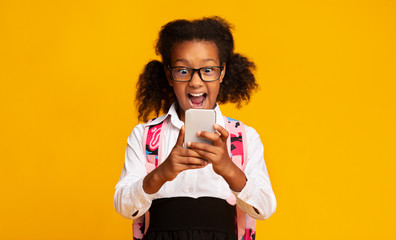 Excited Schoolgirl Using Smartphone On Yellow Background In Studio