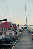 Fototapeta Pomosty - Yachts and boats moored in a harbour at sunrise. Candid people, real moments, authentic situations