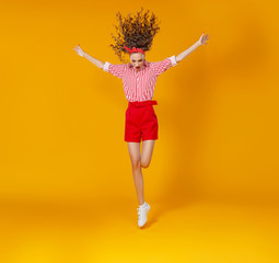 Wall Mural - concept happy emotional young woman in red  jumping   on yellow background