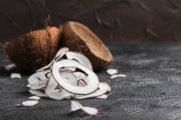 Wall Mural - Coconut chips on a black background, in the background two coconuts