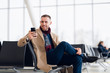 © romankosolapov - young busy man waiting for departure at the airport while using his phone
