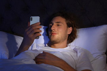 Sticker - Handsome young man using smartphone in dark room at night. Bedtime