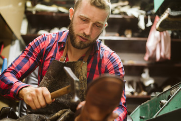 The shoemaker's hands hammer a nail into the heel of the shoe