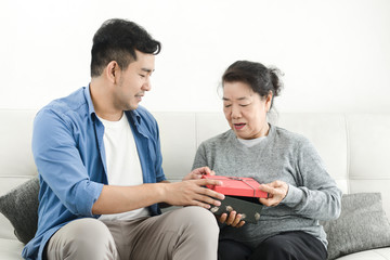 Wall Mural - Happy Asian man giving gift box to his mother for Mother's Day celebration.