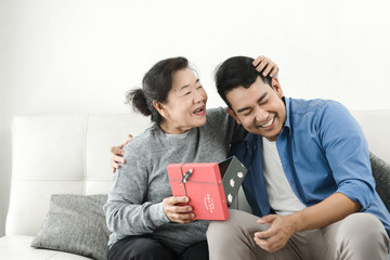 Wall Mural - Happy Asian man giving gift box to his mother for Mother's Day celebration.