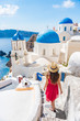 © Maridav - Travel Europe tourist girl walking in Santorini stairs of city streets, famous european destination three blue domes, famous Greek landmark. Oia village, Santorini island, luxury vacation.