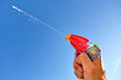 Colorful water pistol spraying out a jet of water in a caucasian male hand in front of  the blue sky of a sunny summer day