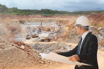 Business engineer planing at construction site with workers on a background of coal mining trucks are driving on the road.