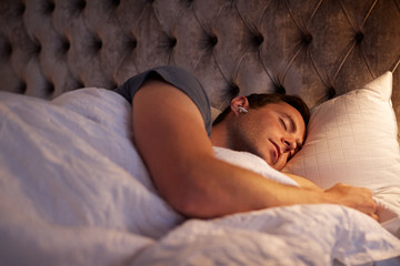 Man Sleeping In Bed Wearing Wireless Earphones Connected To Mobile Phone