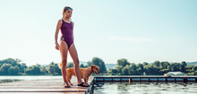 Girl Standing On The Dock With Dog By The River