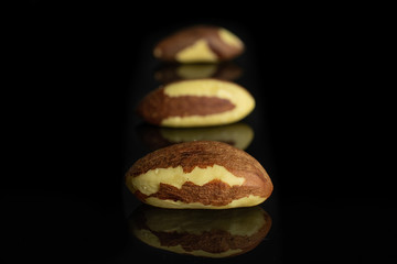 Group of three whole raw brown brazil nut isolated on black glass