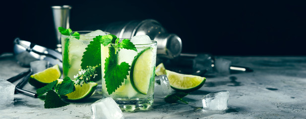 Cocktail Mojito with ice cube in a glass,slice lime, fresh leaf mint, shaker, jigger, metal straw, drops water on glass,Place for text,Banner